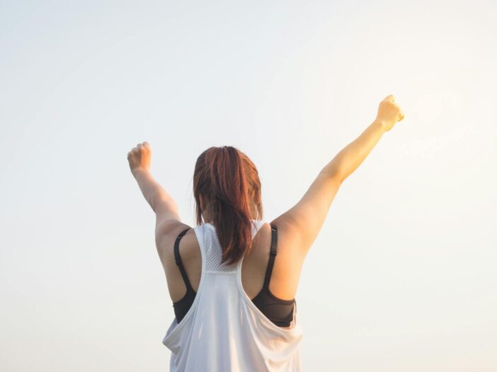 woman wearing black bra and white tank top raising both hands on top